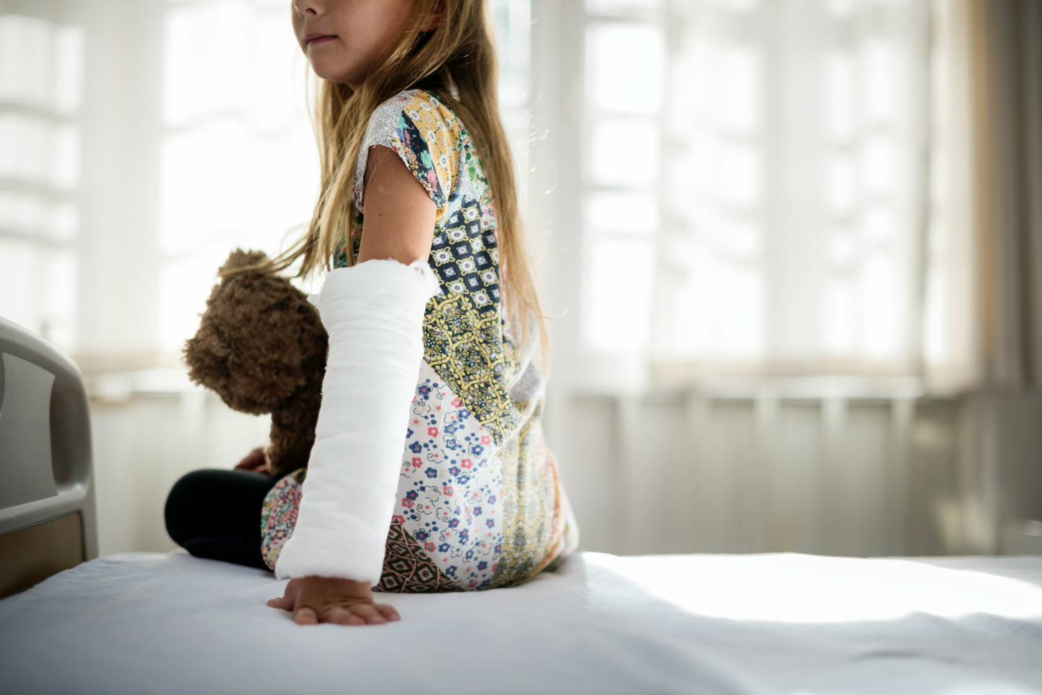 Suma Ubezpieczenia w NNW Szkolnym Dziewczynka z unieruchomioną ręką po złamaniu siedzi na łóżku